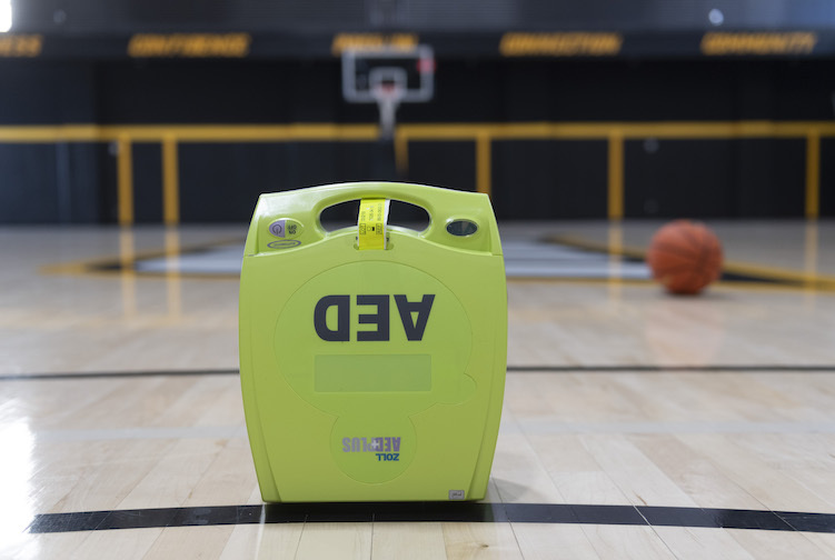 An automatic external defibrillator, known as an AED, is on a basketball court with a basketball behind it. 