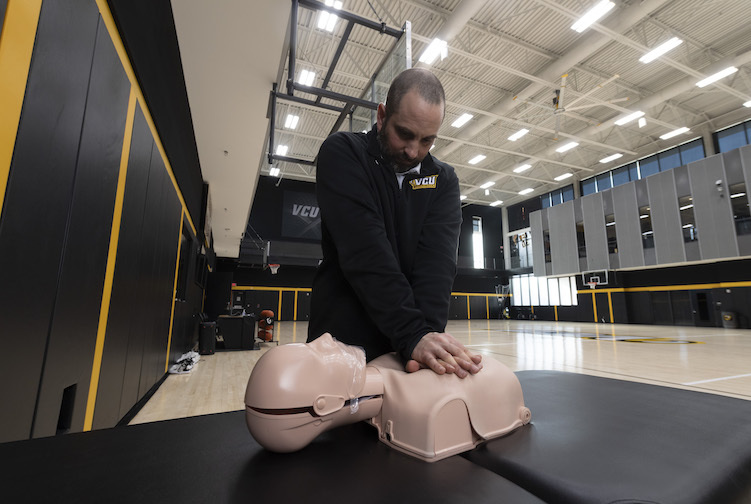 Jeff Collins, VCU's assistant athletic director for sports medicine, stands over a CPR manikin to demonstrate how to do chest compressions in the event of an emergency. 