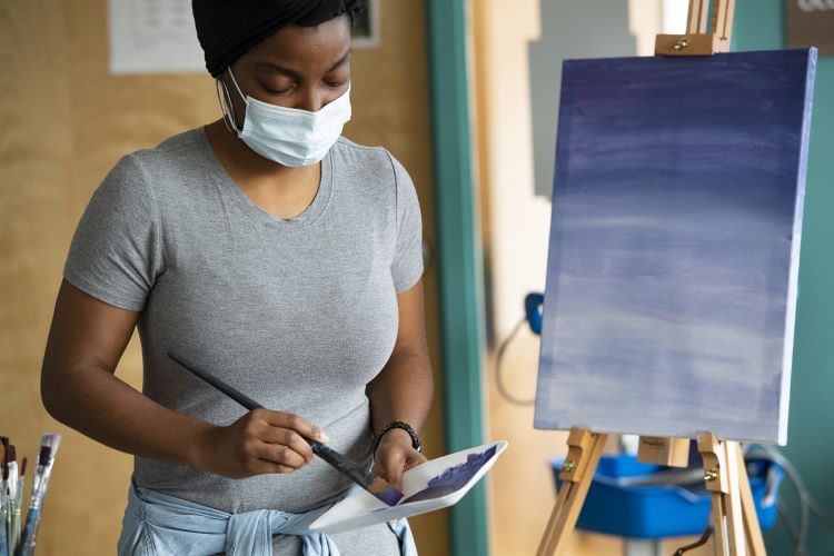 Woman painting a canvas while wearing a face mask