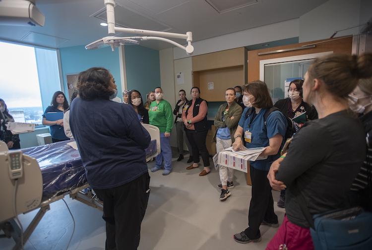 Team members from the Children's Hospital of Richmond stand in a patient room. They are all listening to one woman speak as part of their training. 