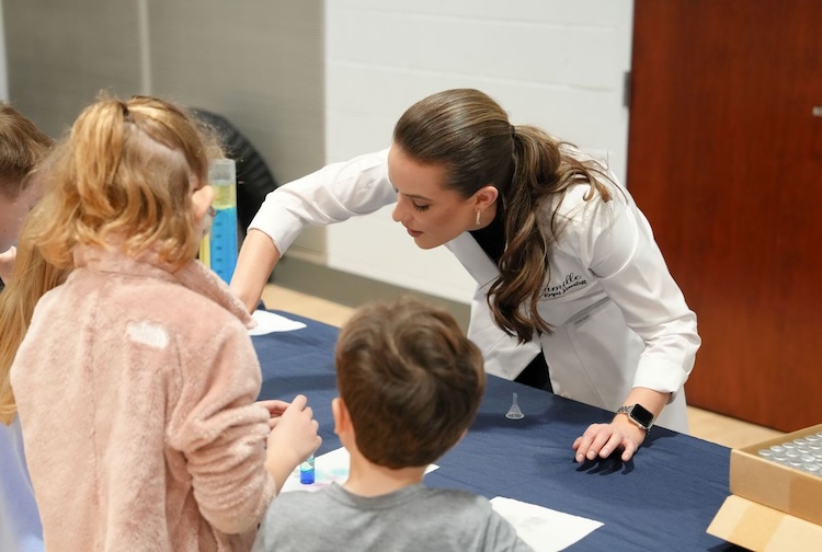 woman in a lab coat doing an experiment with kids