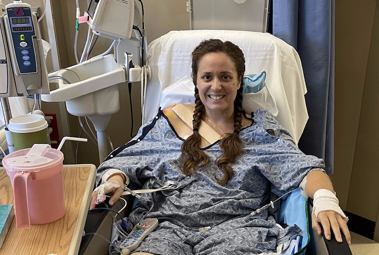 Woman sitting up in a hospital bed. She is smiling and has her hair braided