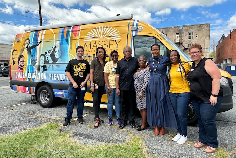 Group of smiling people standing in front of a yellow van. 