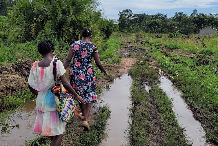 Two women are walking in a field that is filled that has water in it. They are wearing floral dresses and are faced away from the camera. 