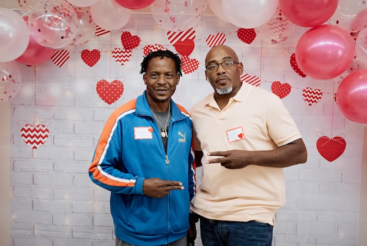 Two men standing together at a photo book that has hearts around it, as part of an event for patients who received heart transplant or heart-related surgery at VCU Health.