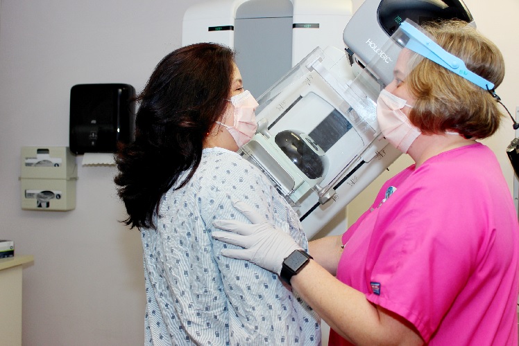 Masked woman receiving mammogram while being assisted by masked nurse