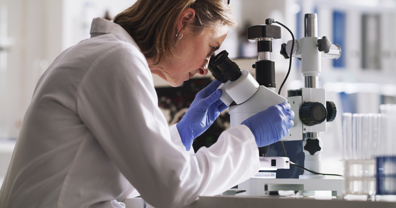 Woman in a lab coat looking into a microscope